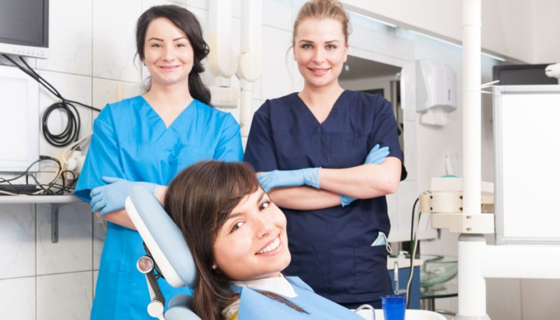 Dentist in Norway: How to Find One You Can Actually Trust 11 Smilende pasient i tannlegestol omgitt av to kvinnelige tannpleiere i uniform på moderne tannklinikk.