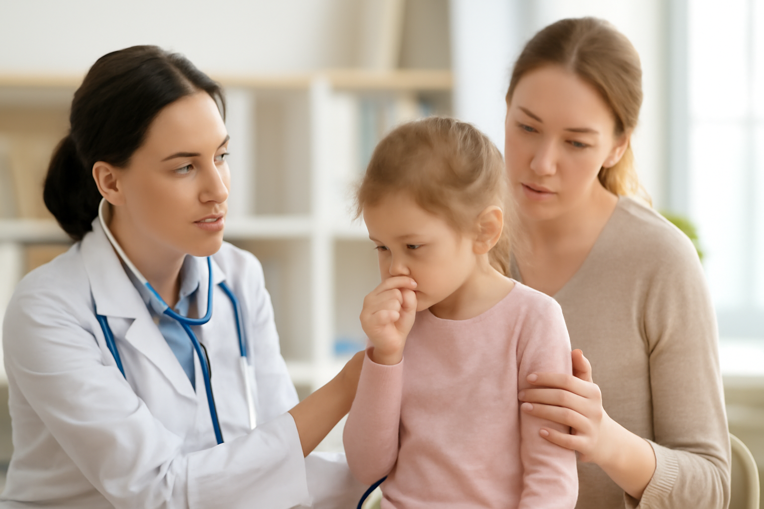 Lege undersøker liten jente som hoster, mor ser på.