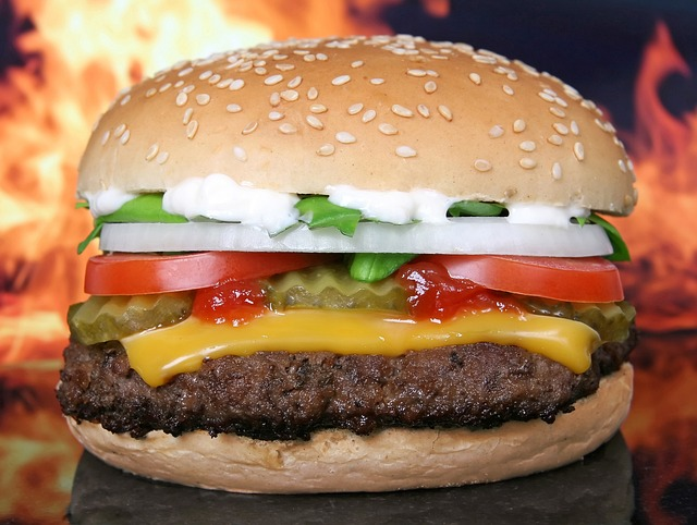 An image of a cheeseburger with flames of fire in the background. 