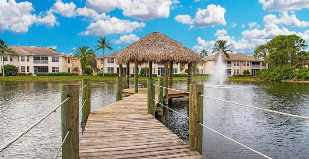The image shows a modern coach home exterior featuring a spacious screened lanai with serene lake views, embodying the ultimate Florida lifestyle in the Coconut Shores community. This beautifully maintained residence is designed for relaxation and enjoyment, perfect for peaceful mornings by the water.