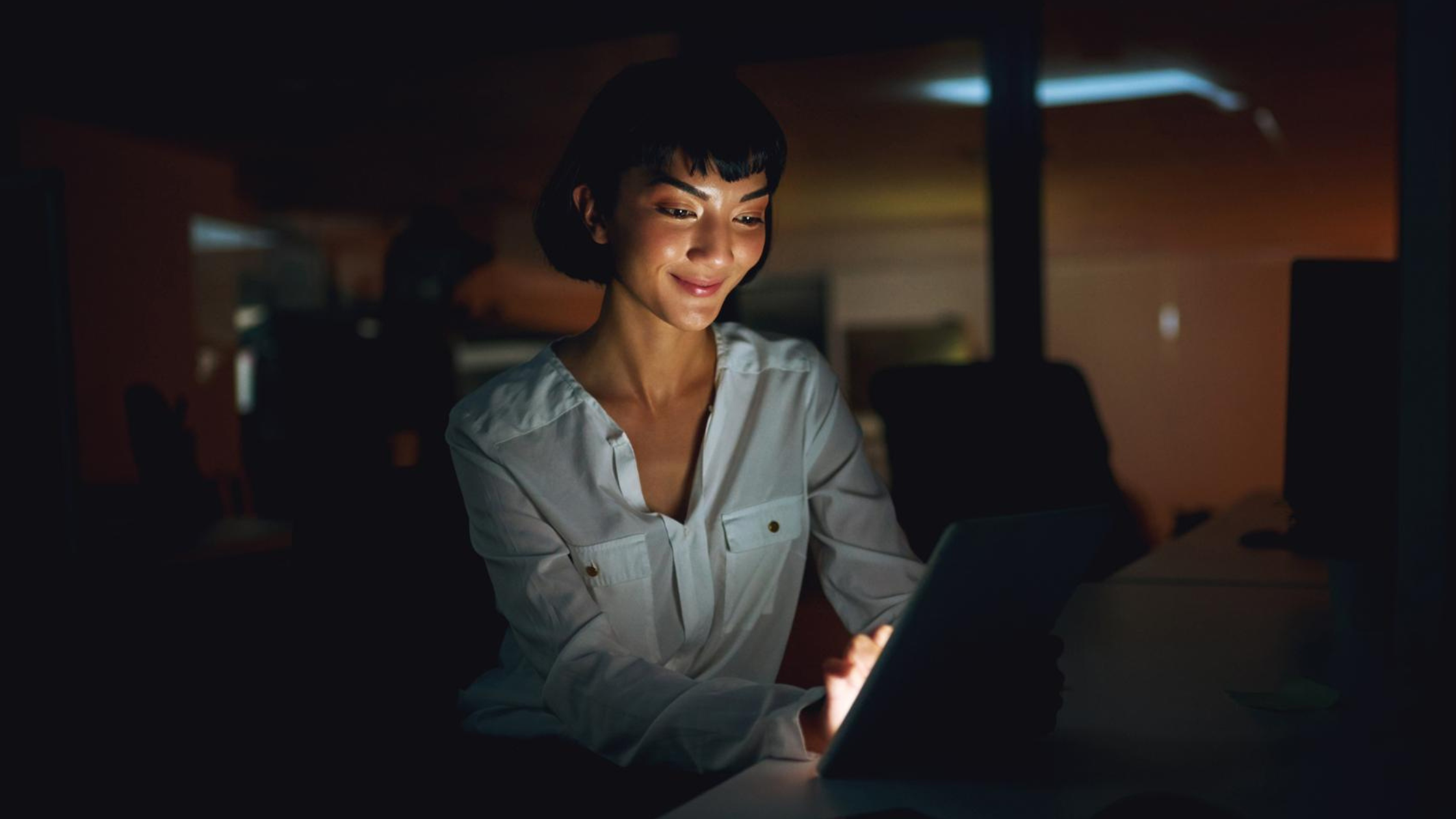 Woman working on a tablet in a dark office, showcasing how cloud PBX providers help maintain business continuity during outages.