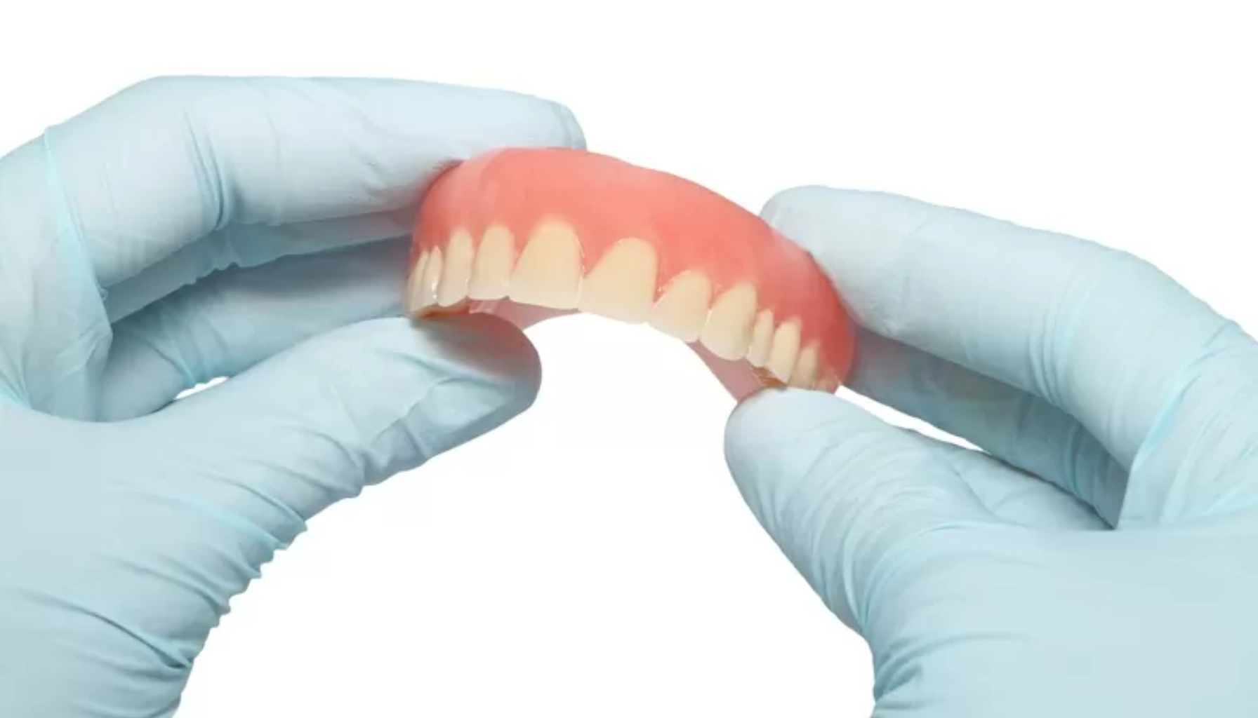 Protese – Alt du bør vite om tannproteser 9 Hender med blå hansker holder et gebiss mot hvit bakgrunn.