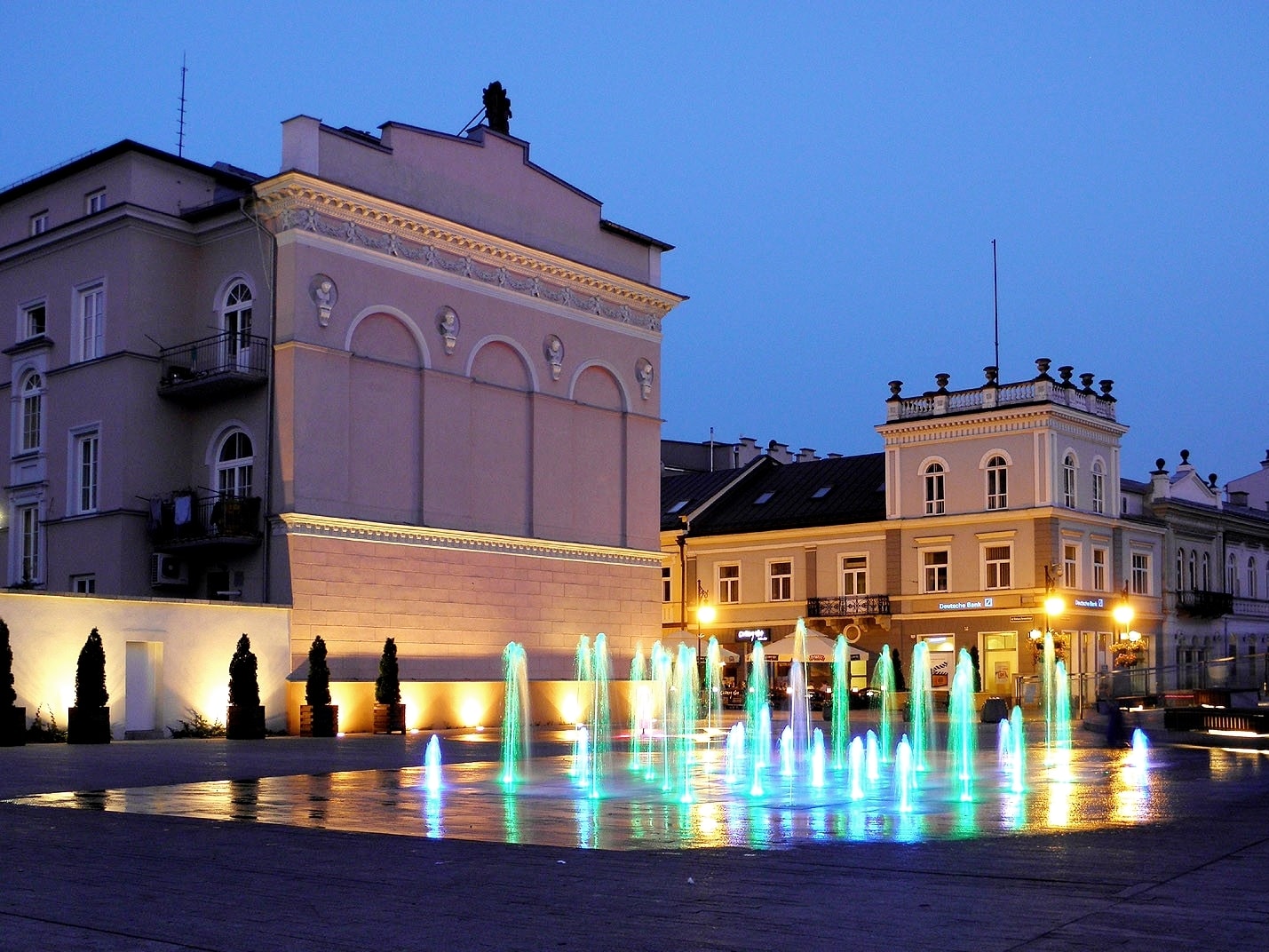 Widok na podświetlaną fontannę w centrum miasty, która zapala się różnymi kolorami po zmierzchu. Źródło: https://commons.wikimedia.org/wiki/File:Fontanny_radom2.jpg