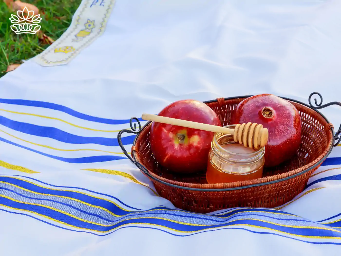 A basket with red apples and a jar of honey on a traditional cloth outdoors - Fabulous Flowers and Gifts, Rosh Hashanah Flowers Collection.
