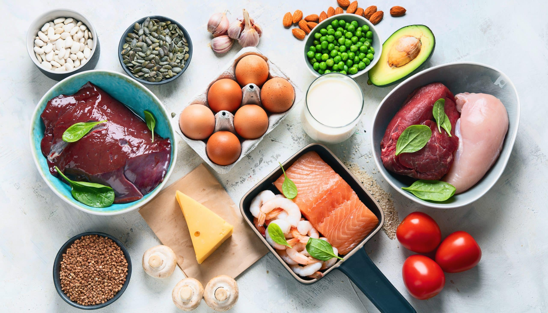 Utvalg av sinkrike matvarer som egg, kjøtt, lever, sjømat, nøtter, frø, ost, melk, belgfrukter og grønnsaker på lyst kjøkkenbord.