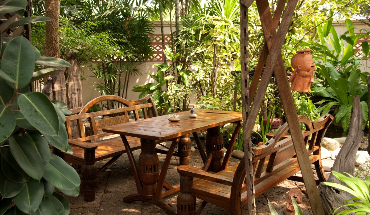 Garden furniture - dark wood, heavy table and benches on leafy garden patio 