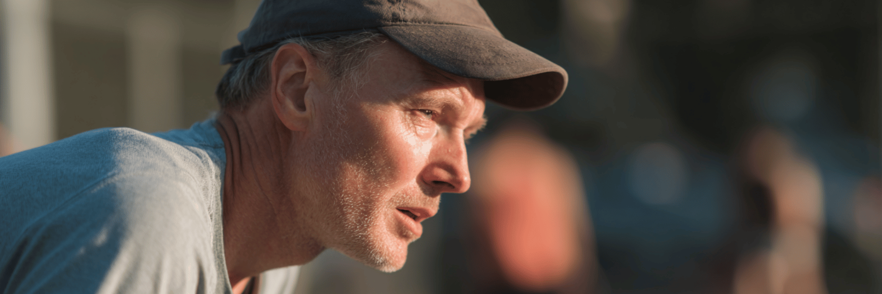A close-up profile of a focused older man wearing a baseball cap, his face highlighted by the sun.