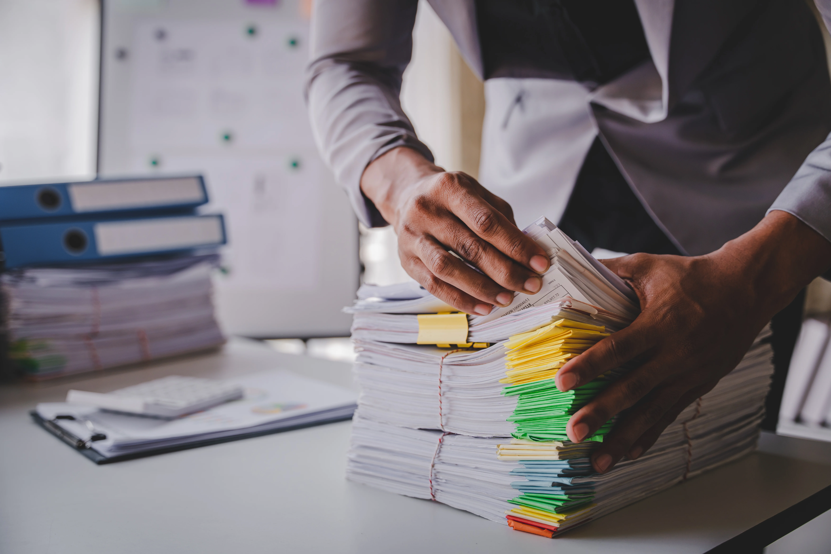 A person holding a stack of paper documents and a pen