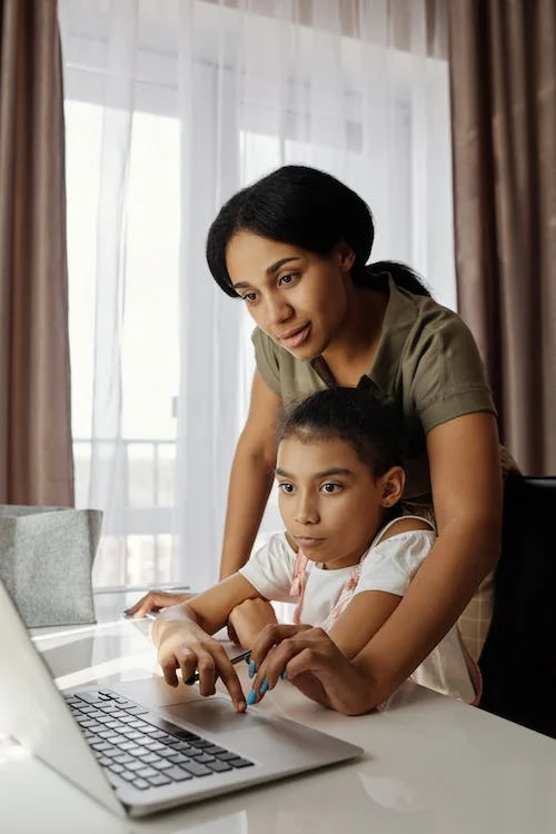 A smiling mother is helping her curious child search the internet on laptop. 