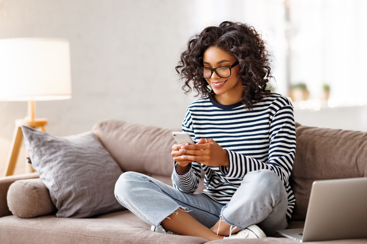 Woman in a blue and white striped shirt smiling and looking at her phone.