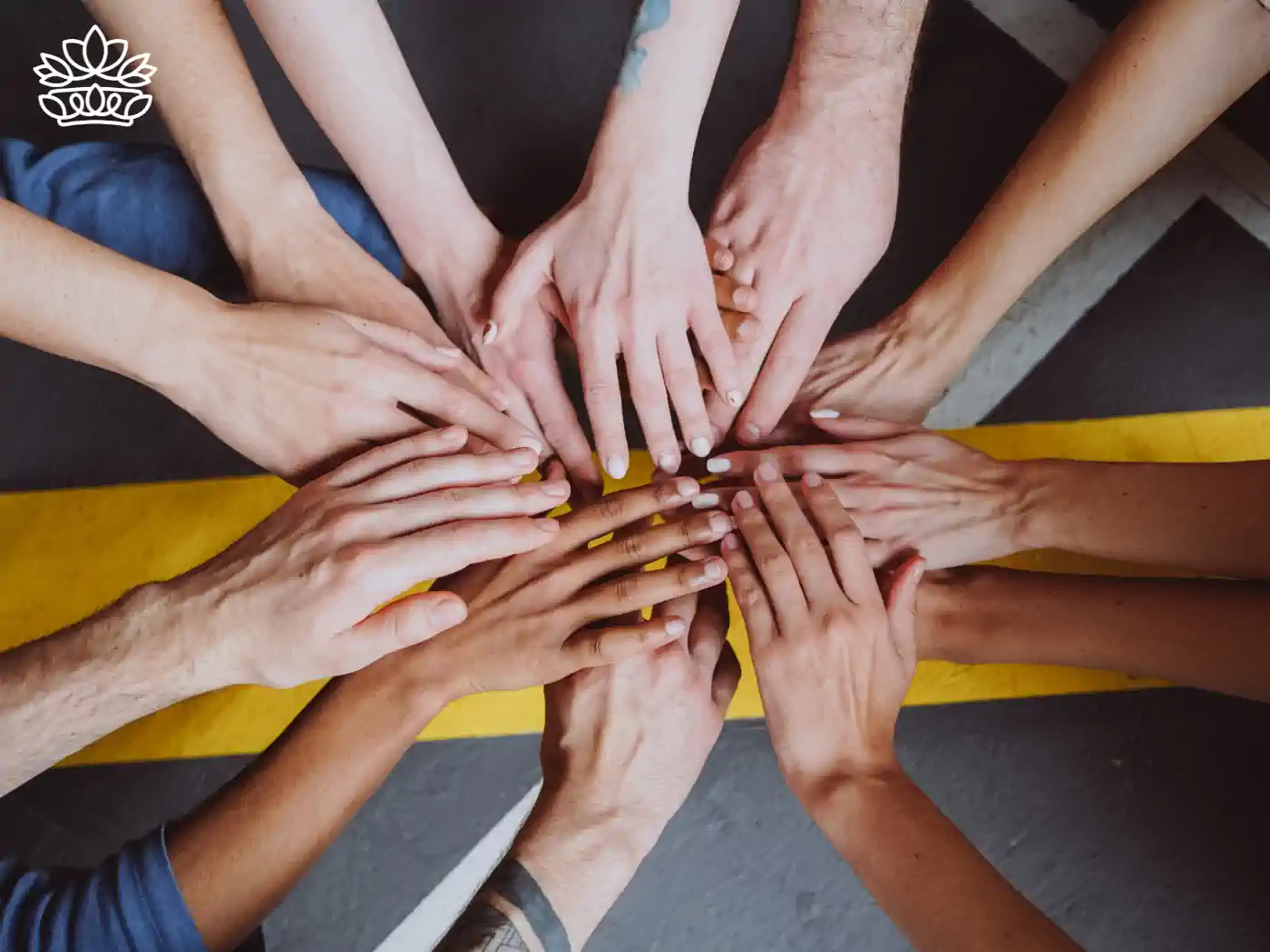 Overhead view of a diverse group of hands, representing different ethnicities, coming together in a unified circle on a grey background, symbolising teamwork and unity in the workplace. Fabulous Flowers and Gifts. Team Gifts. Delivered with Heart.