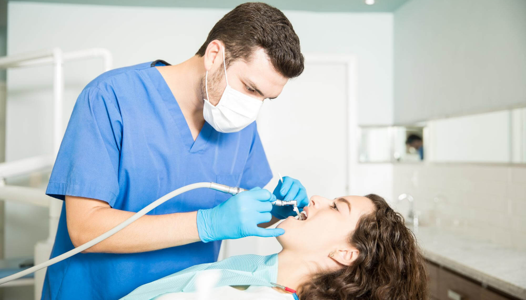 Tannlege som behandler en kvinne med utstyr for tannrens i klinikken.