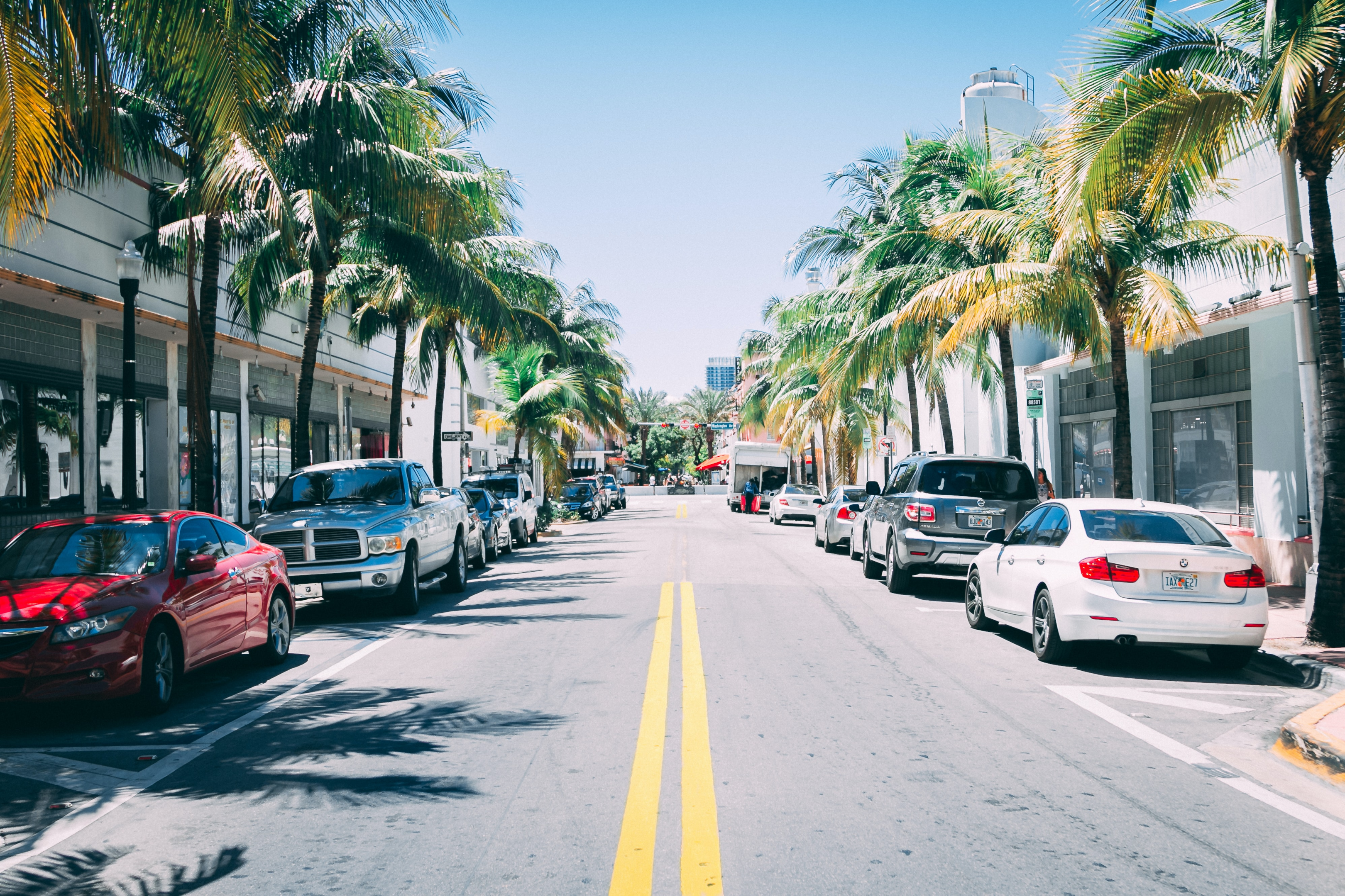 A two lane street in Miami with cars parked on each side of the road. We are the #1 Florida car shipping company.