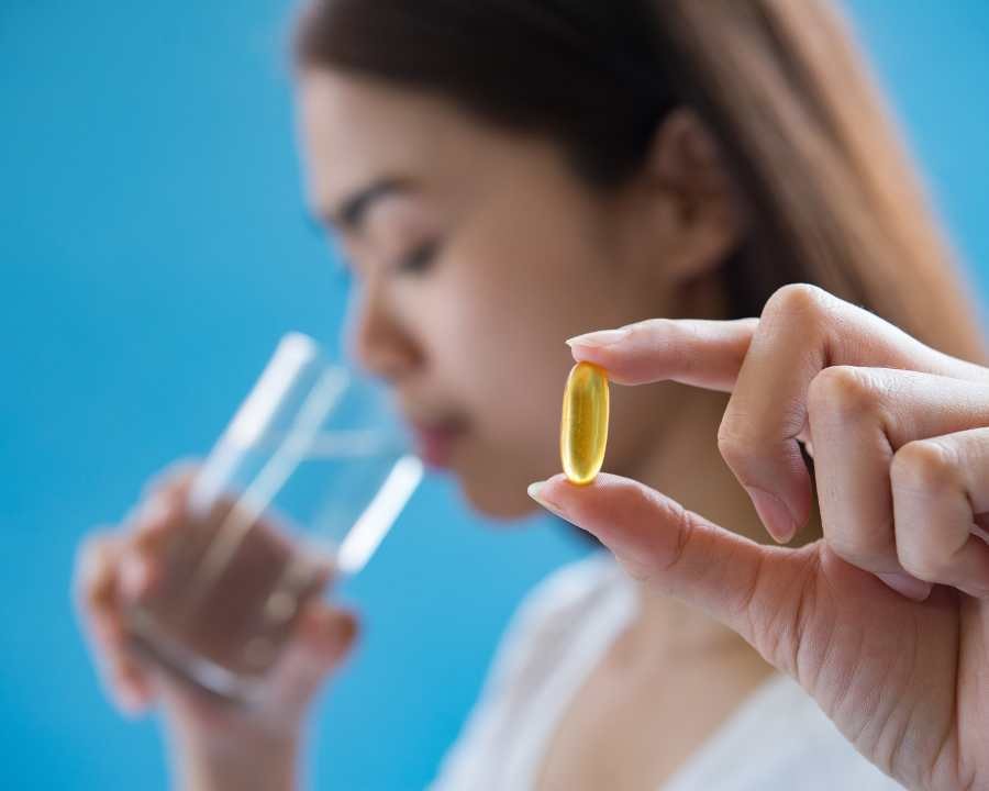 Woman holding supplement softgel capsule with glass of water, ready to take – The Good Stuff nutrition and wellness range