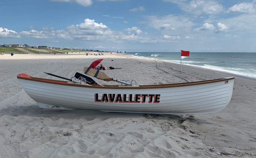 A white lifeguard boat labeled “Lavallette” rests on the sandy beach under a blue sky, with a red flag and ocean waves in the background. Photo courtesy of Ocean County Business Development & Tourism.