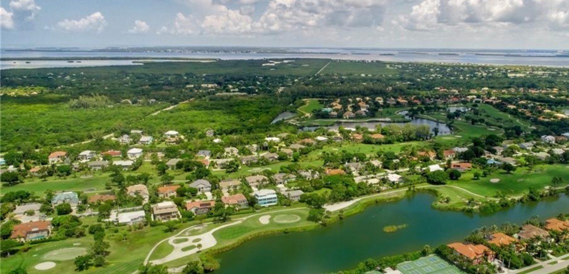 An aerial view reveals the beautifully landscaped grounds of the Beachview Country Club Estates, showcasing a stunning golf course intertwined with luxurious homes. The scene captures the essence of Sanibel Island's tropical lifestyle, featuring vibrant greenery and serene outdoor spaces ideal for relaxation and enjoyment.