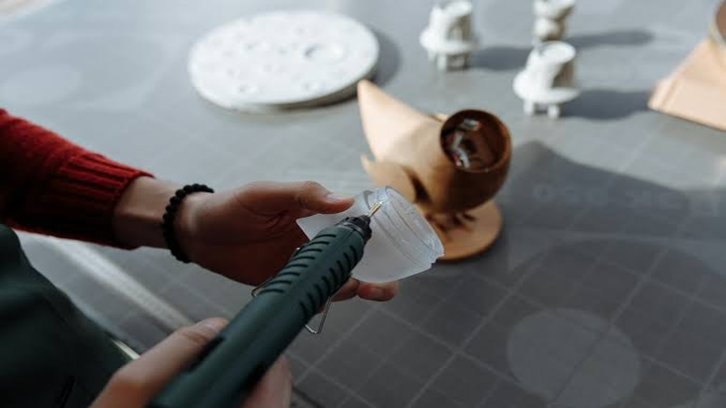 Person using a hot glue gun to assemble a plastic part for a model or prototype on a workbench
