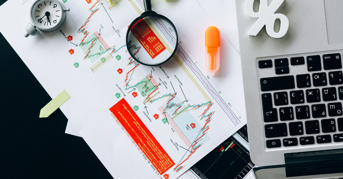 NDIS Housing - A graph chart document showing candle sticks of risks and returns and there is a magnifying glass, MacBook and a clock on the table