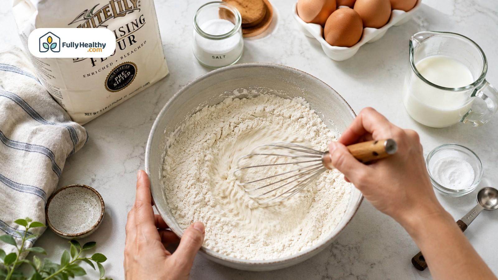 Hands whisking self-rising flour mixture with eggs, milk, salt, and baking powder