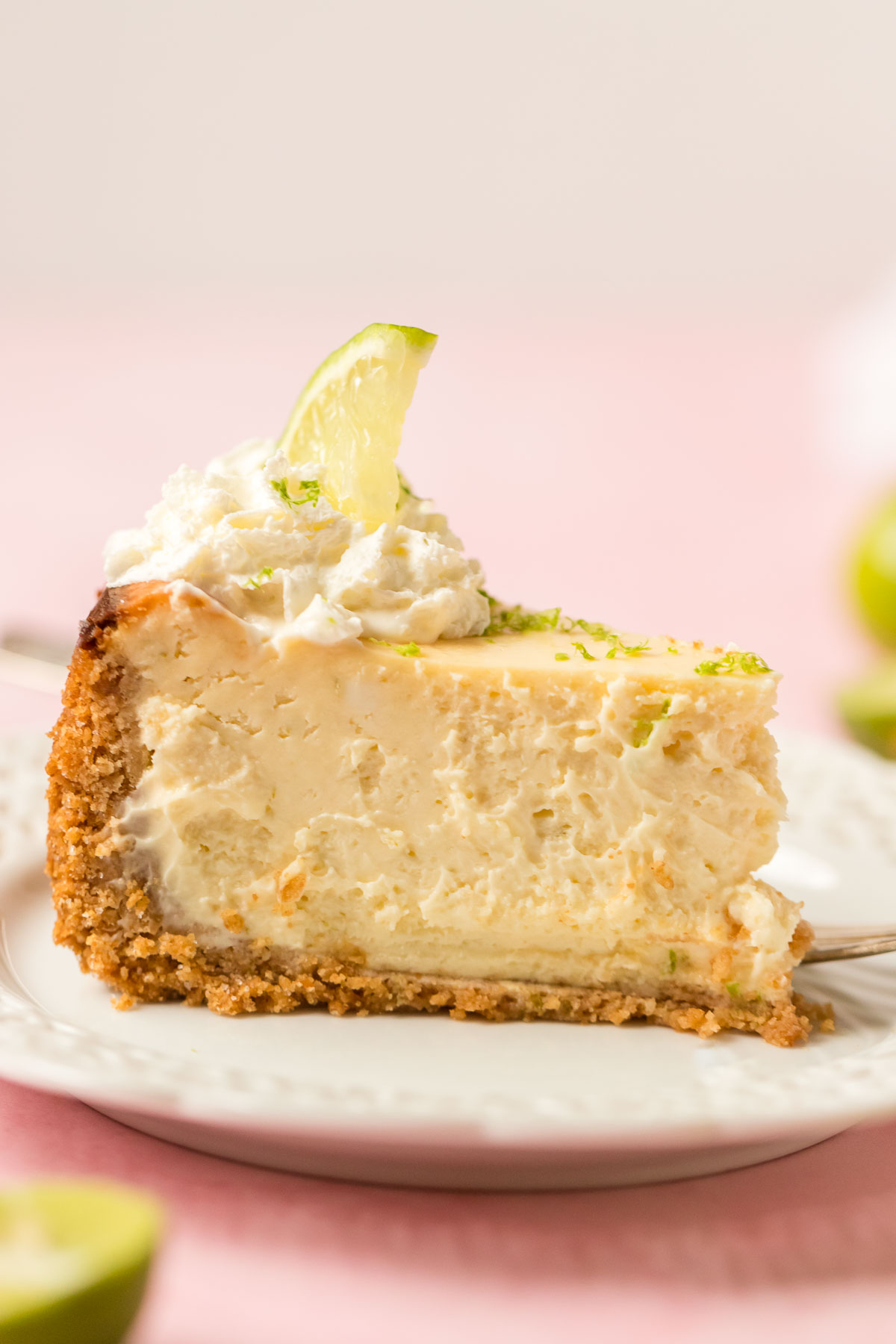 slice of key lime cheesecake topped with whipped cream and lime slices on a plate