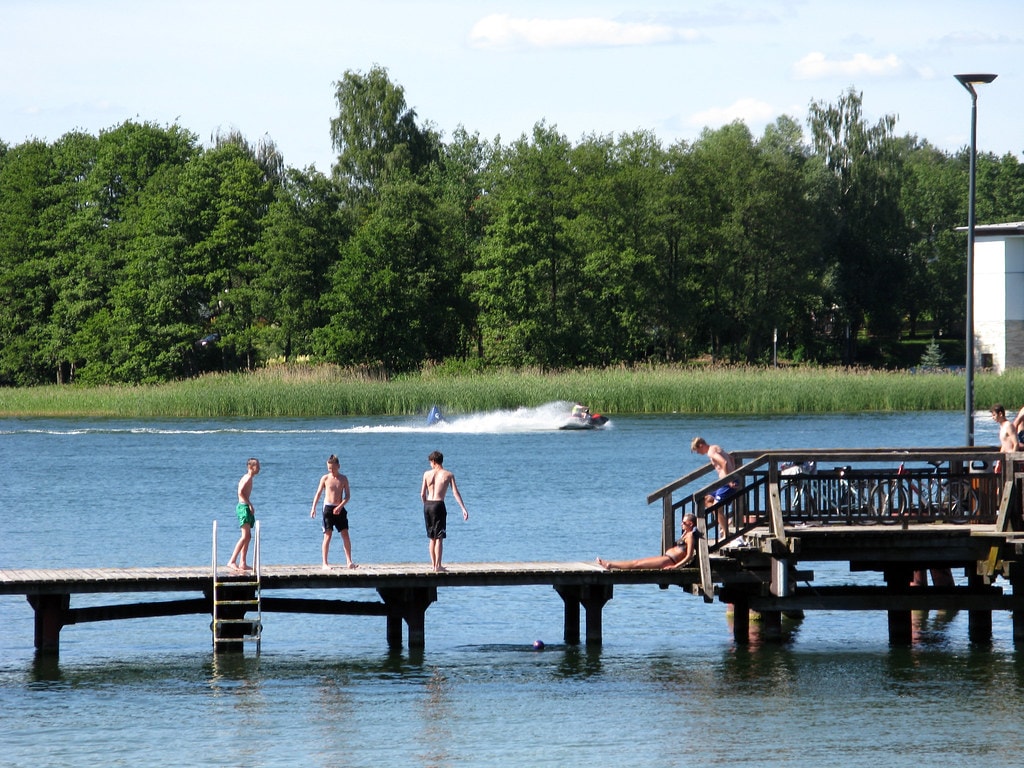 Plaża miejska przy jeziorze Ukiel i pomost, na którym stoją młodzi chłopcy. Źródło: https://www.flickr.com/photos/160950421@N07/29978989467