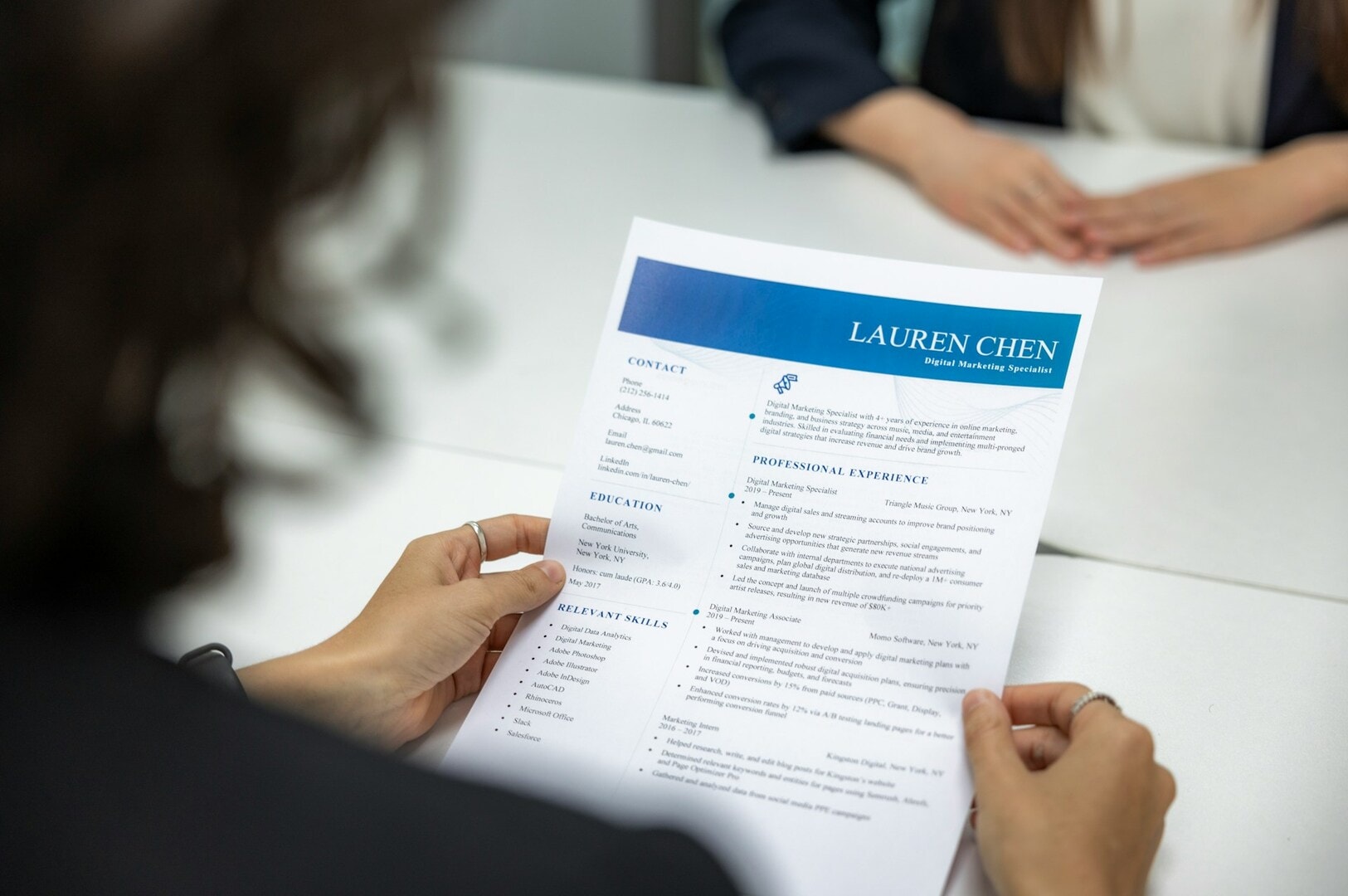 A person holds a resume in front of a desk, symbolizing the job hunting process.