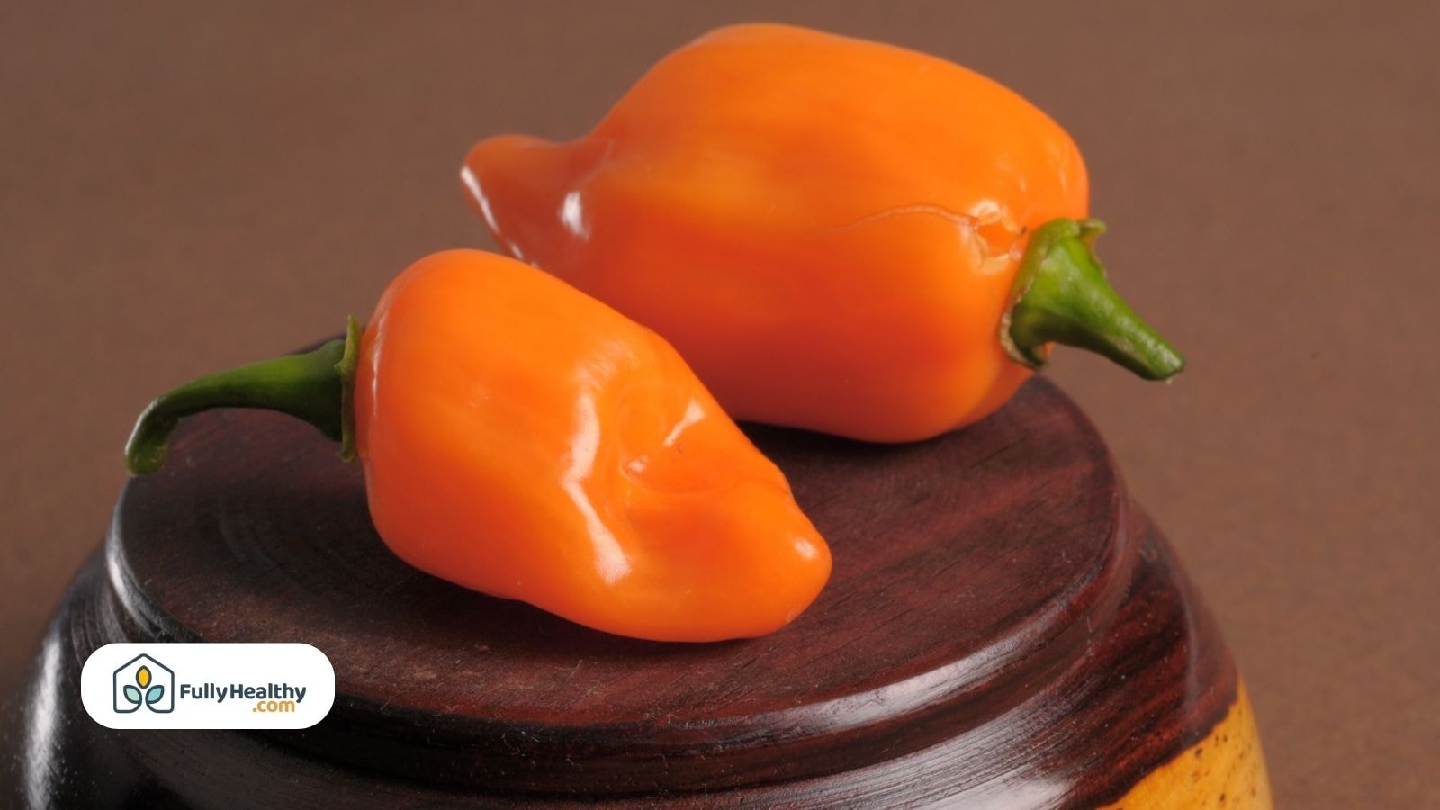Two bright orange habanero peppers on dark wooden base