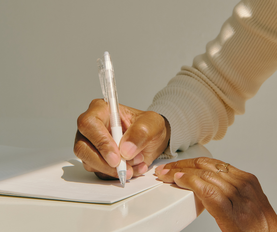 a woman wearing a beige sweater writes in a notebook 