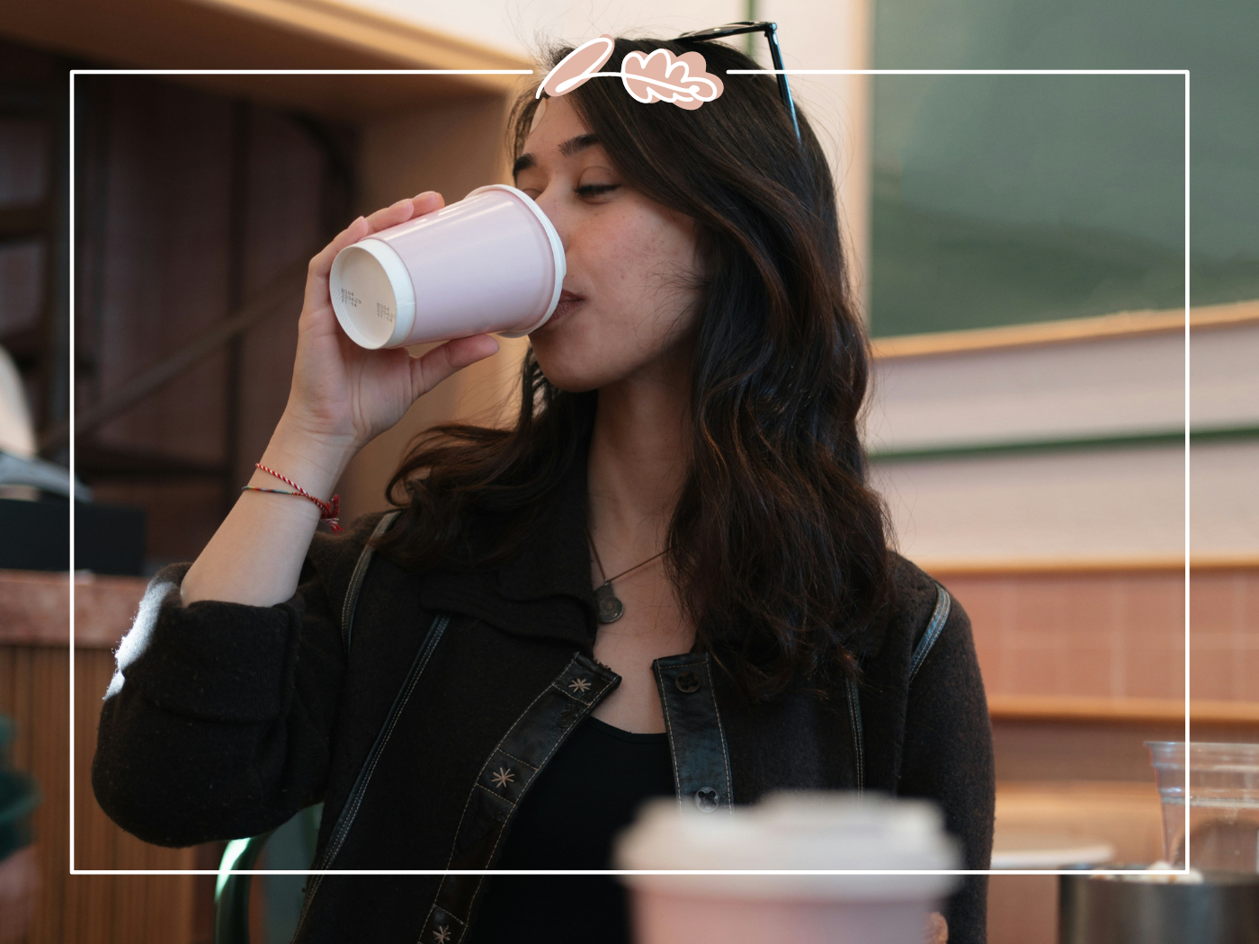 Woman sipping coffee from a paper cup inside a café. Fabulous Flowers and Gifts