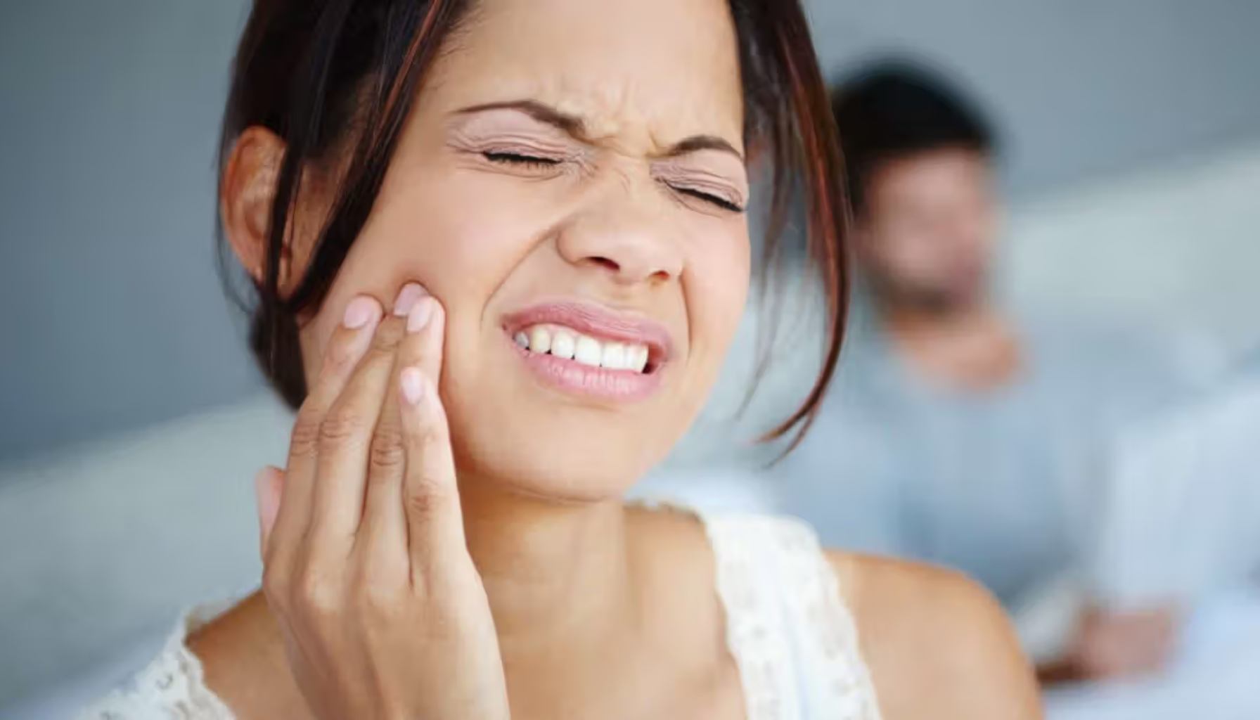 Kvinne holder seg til kinnet – akutt tann- eller kjevesmerte.