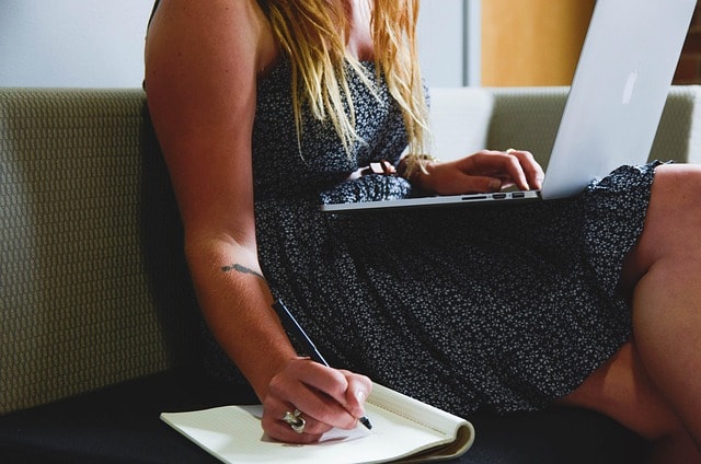A woman typing on her laptop and writing in a note