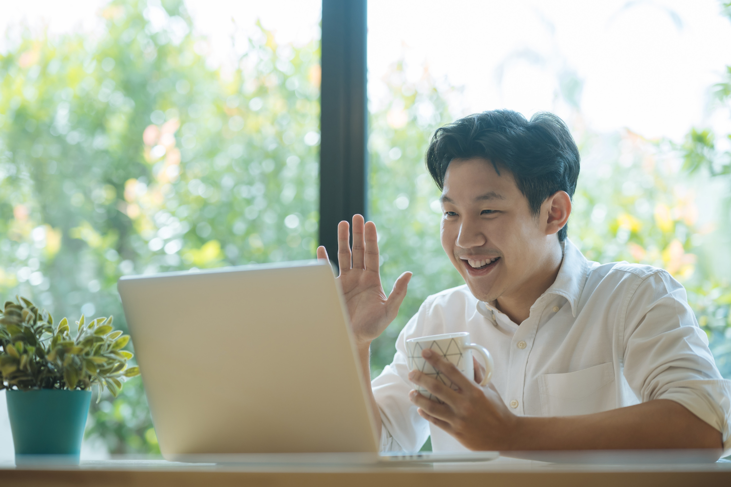 A virtual assistant on a video call, saying hi on laptop screen while holding a coffee cup.