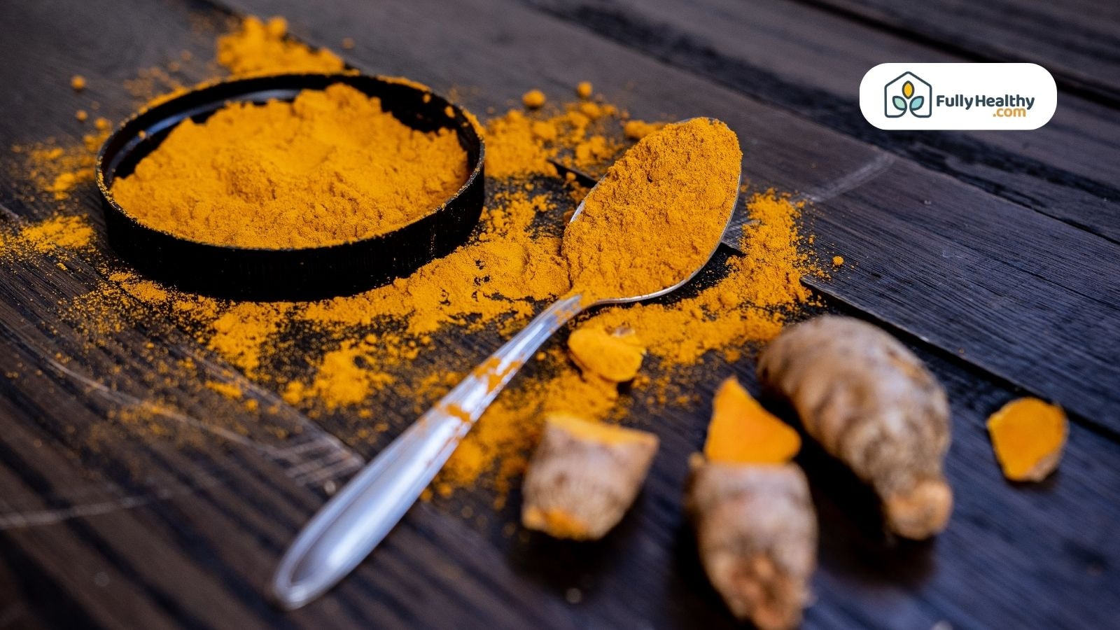 Spoonful of turmeric powder with scattered spice and sliced turmeric root