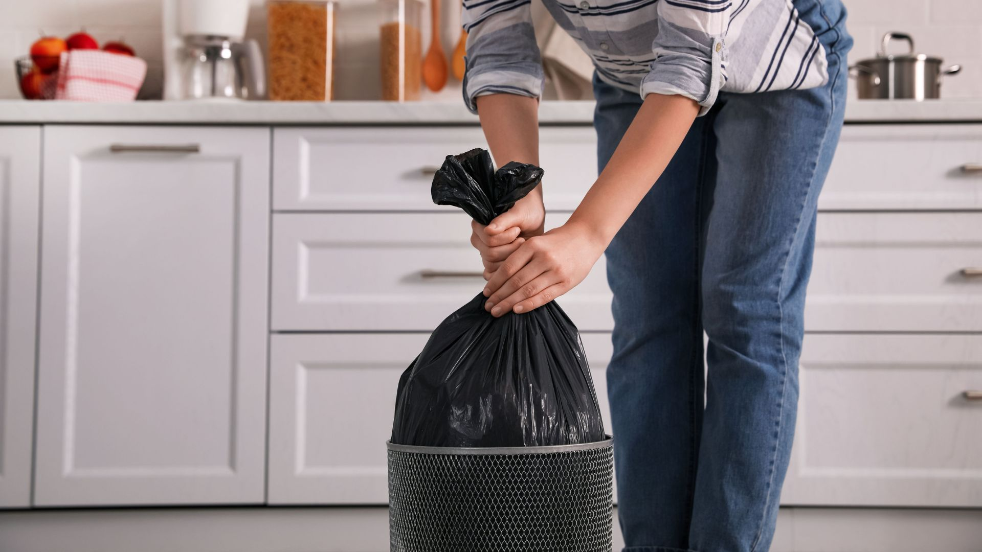 An image of a woman disposing of trash from a waste basket to prevent flies.