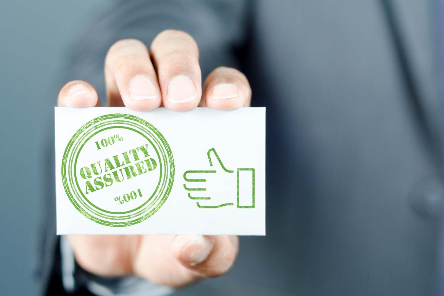 Hand holds a card with a green stamp that reads "100% Quality Assured" and a thumbs up icon.