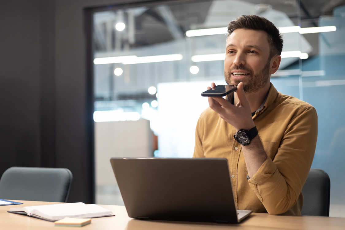 Man speaking into a smartphone in an office, illustrating hands-free voice AI tools for broker research.