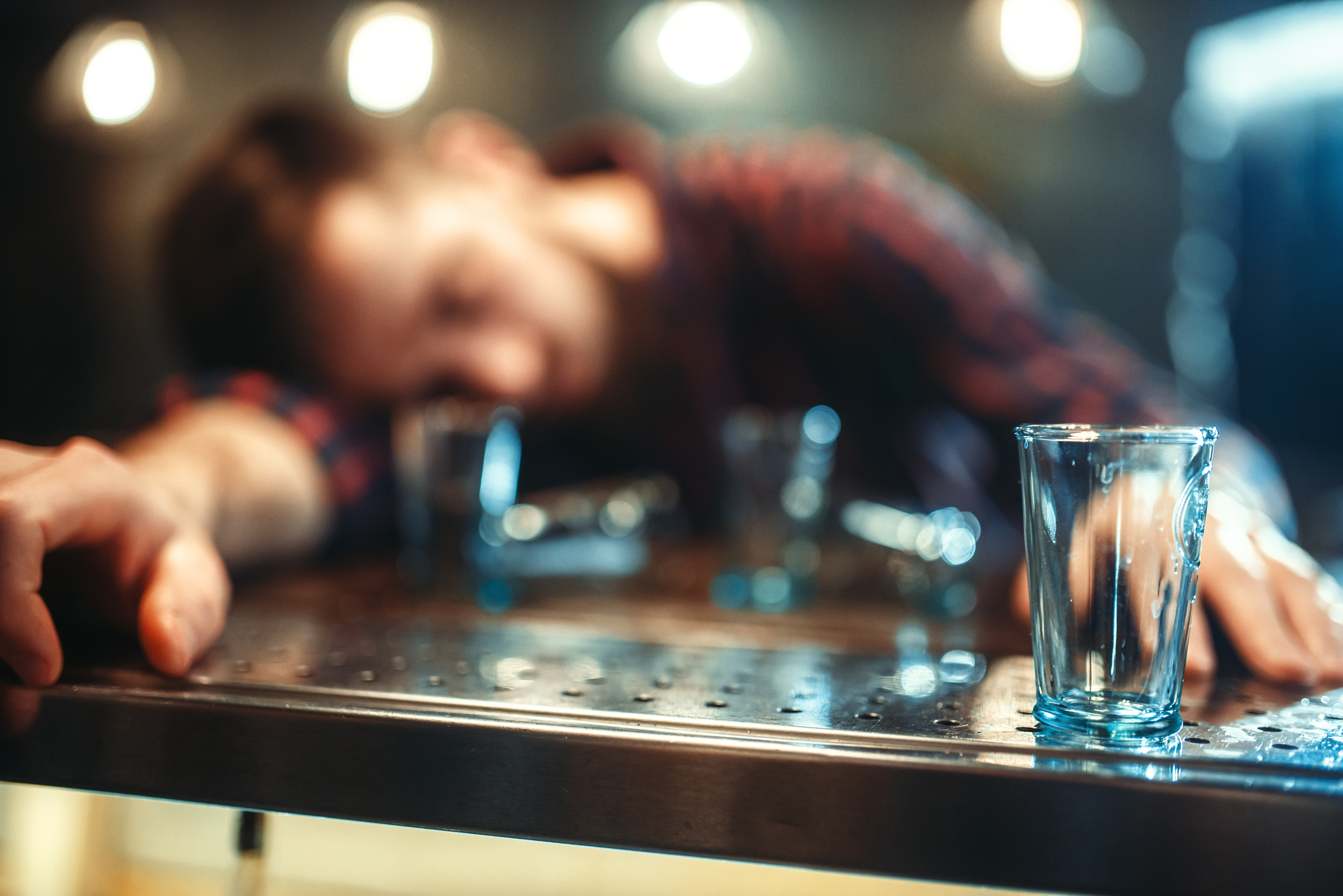 Man dozing off at the bar, empty glasses around him.