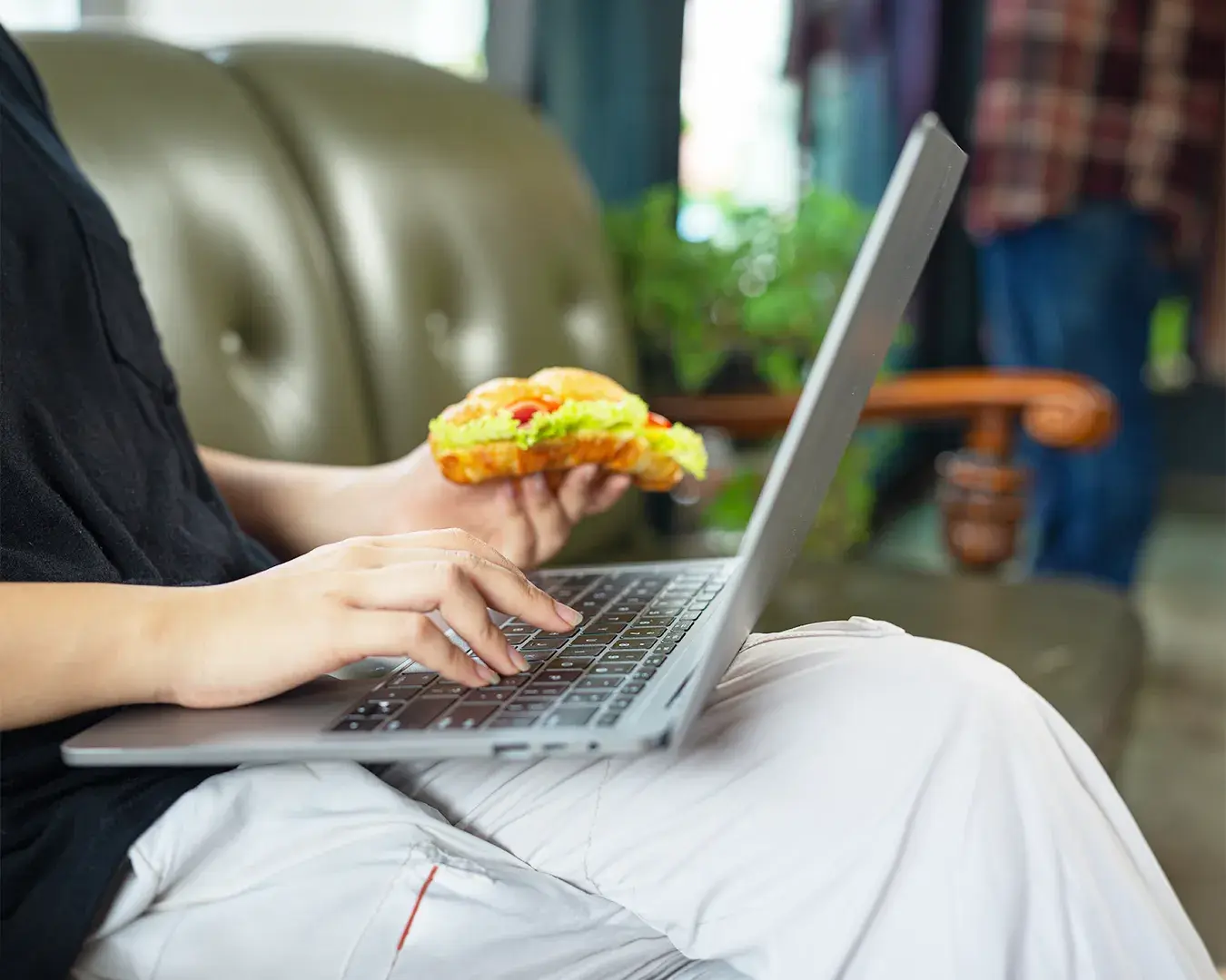 Customer ordering food online from a laptop while enjoying a sandwich, illustrating restaurant online ordering, direct ordering platform, and convenient food delivery alternatives.
