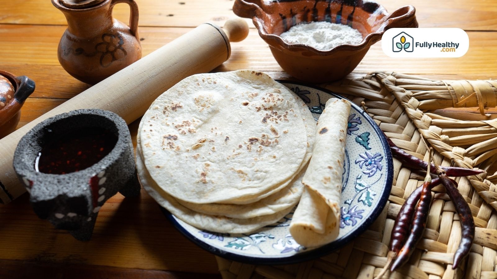 Plate of tortillas with one rolled surrounded by traditional Mexican cooking items and ingredients
