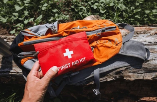 Hand holding red first aid kit outdoors