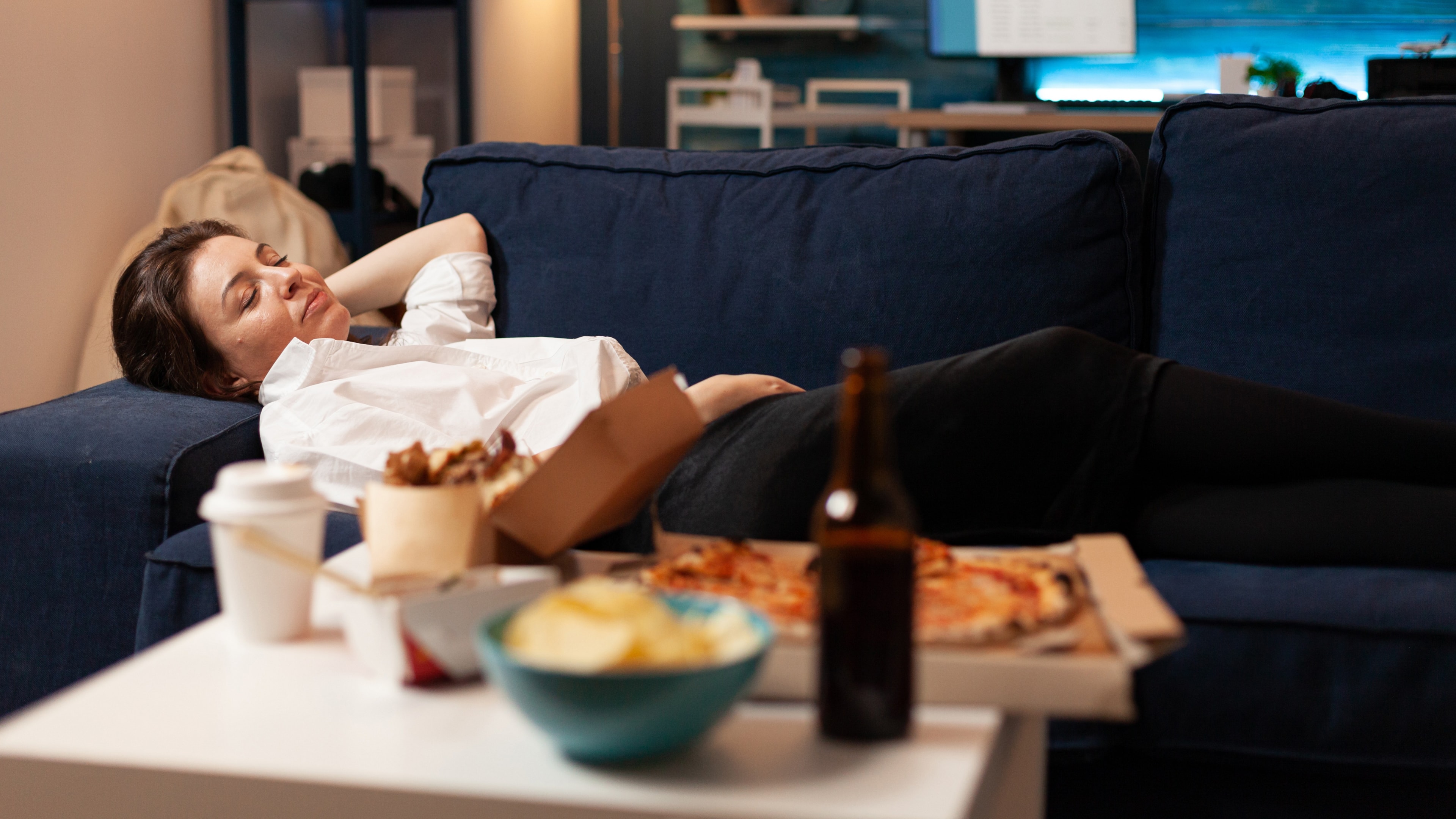Czego nie jeść na noc? Na zdjęciu kobieta spożywająca fast food i alkohol na kolację. To niezdrowe!