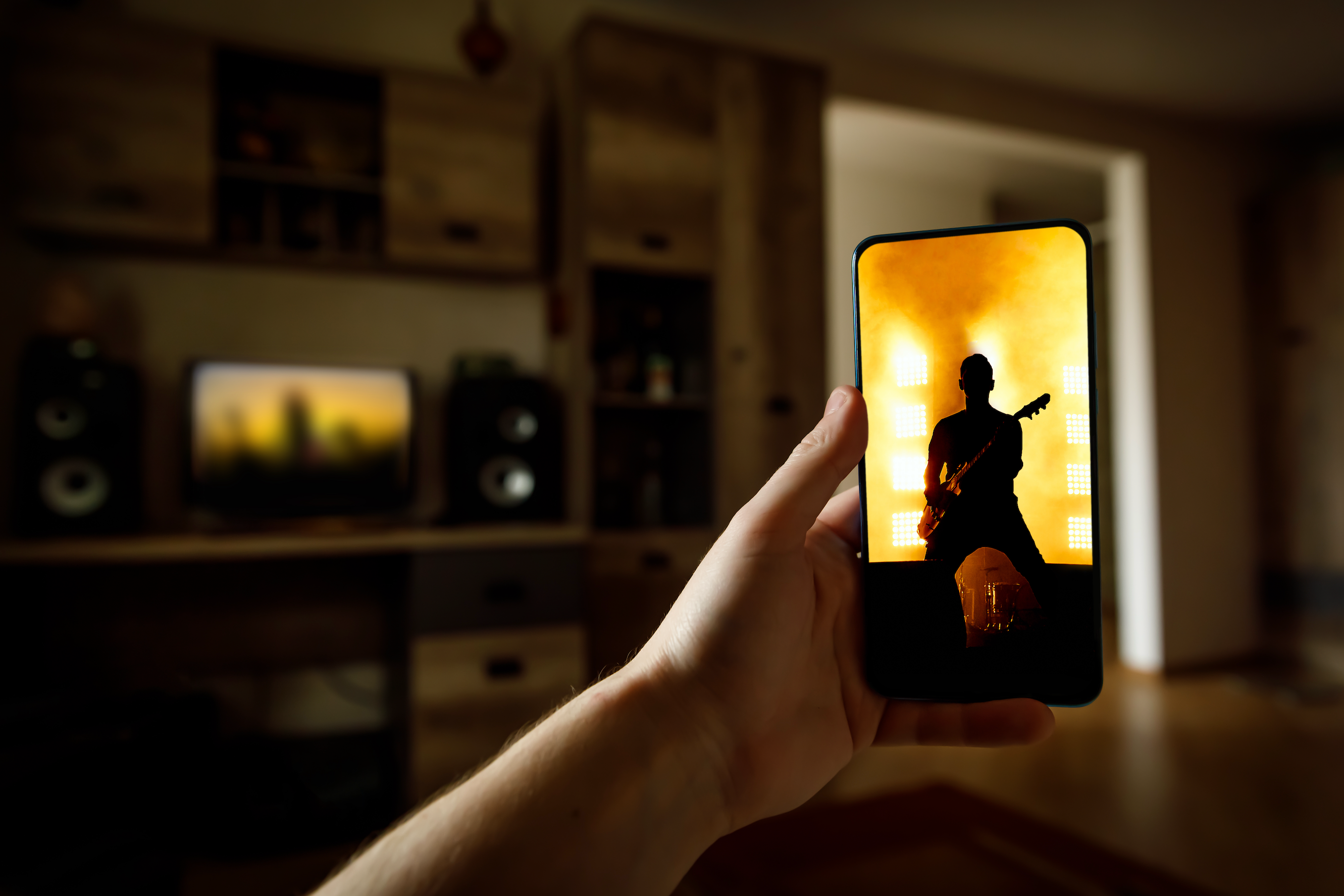 a hand holds a phone streaming live music that matches the same screen on the television in the background
