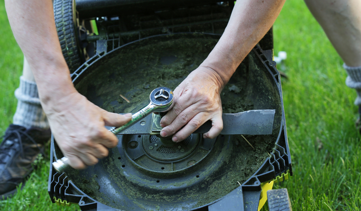 A figure using a wrench to remover a rotary  mower blade