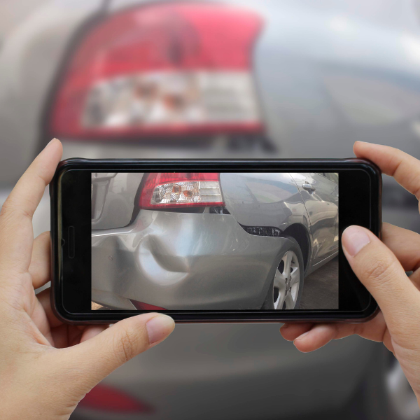 A photograph showing a person taking photos and notes at a car accident scene.