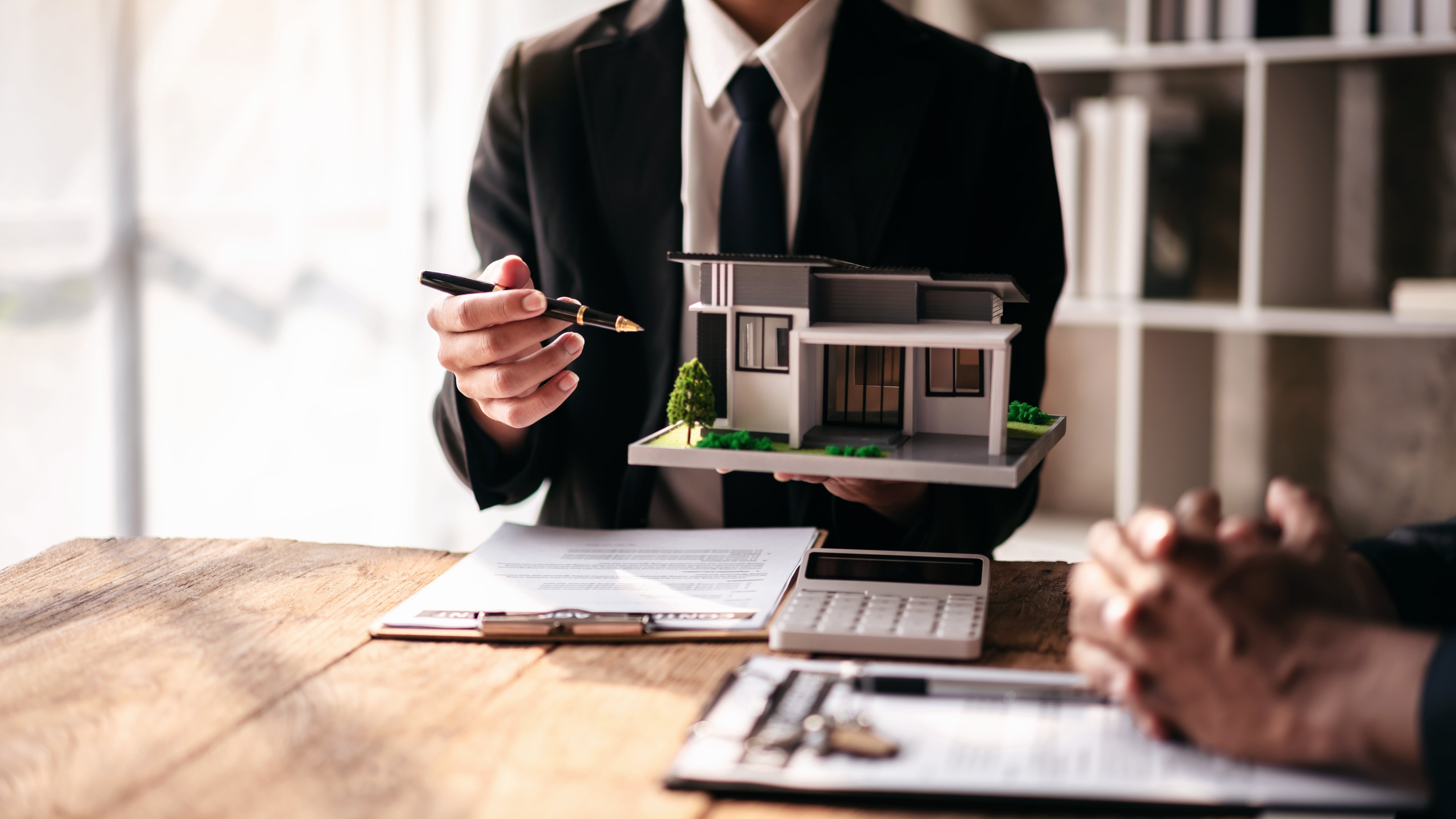 A man is holding a model house and a pen on a table, sunshine coast, maroochydore, email, qld