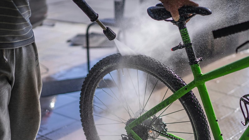 cleaning the rear wheel of a green bicyle using a high pressure water