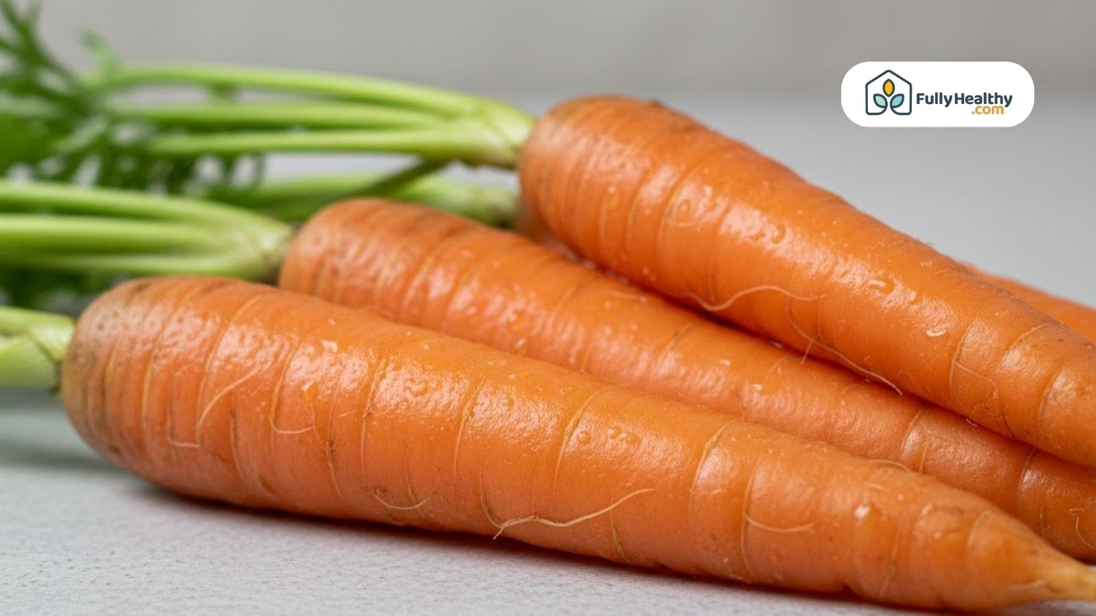 Fresh whole carrots with green tops displayed on a neutral surface.