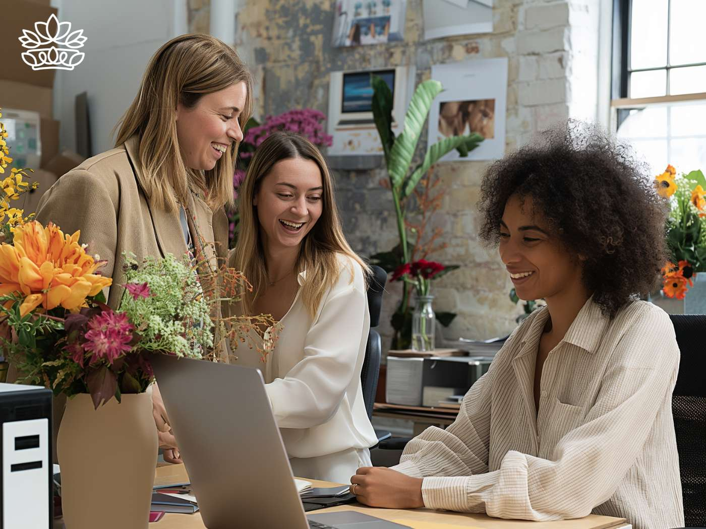 Three colleagues sharing a joyful moment at a desk adorned with vibrant floral arrangements, epitomizing the workplace harmony at Fabulous Flowers and Gifts.