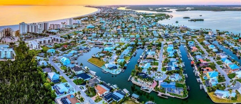 The image depicts a luxurious waterfront home in Fairview Isles, showcasing a private dock that provides direct access to the gulf access canal. The property features modern luxury elements, including a heated pool and beautifully designed interiors, perfect for enjoying the serene lifestyle near Fort Myers Beach and its pristine white sandy beaches.