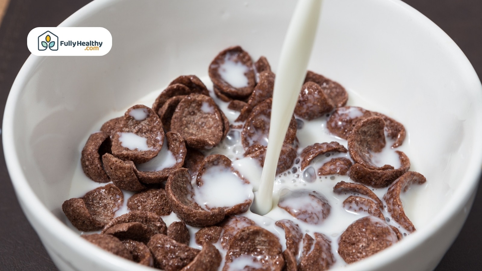 Chocolate cereal with milk being poured into white ceramic bowl